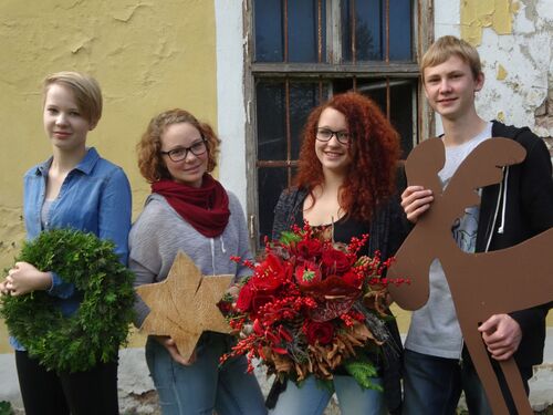 4 Schüler der Schule Ritzlhof mit floristischen Werkstücken, Holzstern, rotem Gesteck, grünem Kranz, Figur aus Eisen