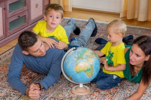 Vater, Mutter und zwei Kinder liegen am Teppich und schauen sich einen Globus an
