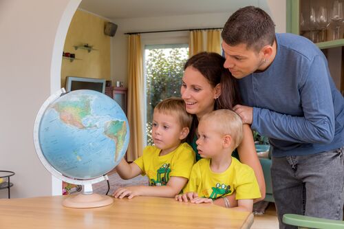 Vater, Mutter und zwei Buben betrachten einen Globus