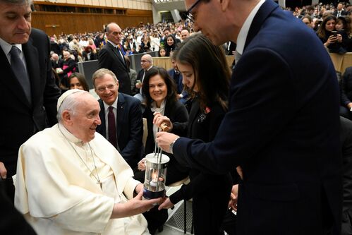Großer Saal mit Publikum, im Vordergrund Papst Franziskus, sitzend, vor ihm stehend Sarah Noska, die ihm eine Speziallaterne, in der sich eine kleine Flamme befindet, überreicht