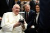 Papst Franziskus, sitzend, schaut voller Freude auf das Friedenslicht, das er in Händen hält, hinter ihm, sitzend, Landeshauptmann Mag. Thomas Stelzer mit Gattin