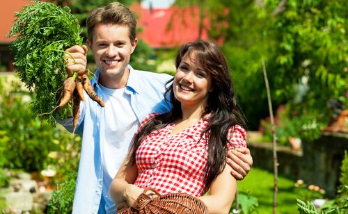 Ein junges Paar freut sich über selbst angebaute Karotten.