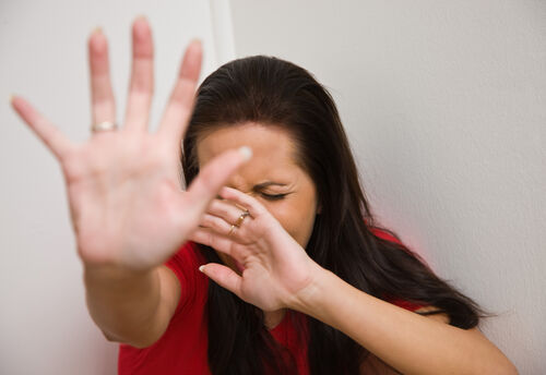 Frau hält sich schützend eine Hand vor das Gesicht und wehrt mit der anderen ab.