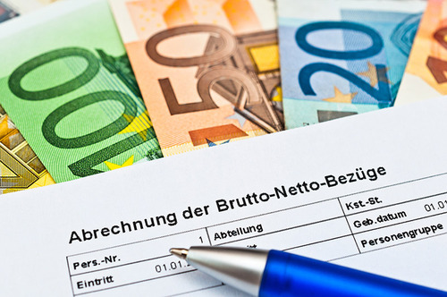 Ein Gehaltsabrechnungszettel und ein blauer Kugelschreiber liegen auf mehreren Euro-Scheinen
