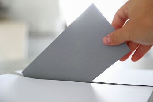 Eine Person wirft ein Kuvert mit Stimmzettel in eine Wahlurne.