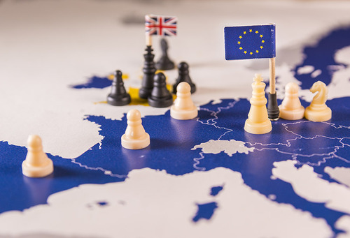 Auf einer Europakarte stehen mehrere weiße und schwarze Schachfiguren sowie eine EU-Flagge und eine Flagge des Vereinigten Königsreichs Großbritannien und Nordirland