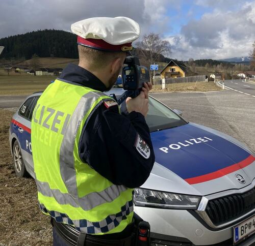 Polizist steht vor Polizeiauto mit Laserpistole in der Hand