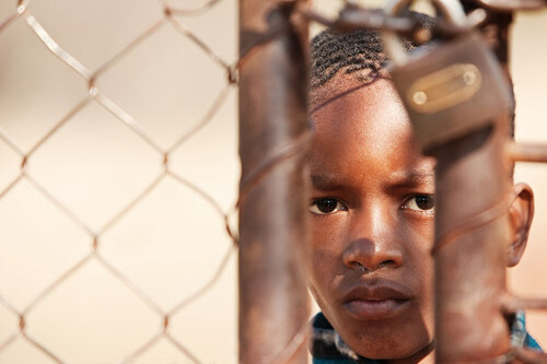 schwarzes Kind steht hinter einem verschlossenen Zaun