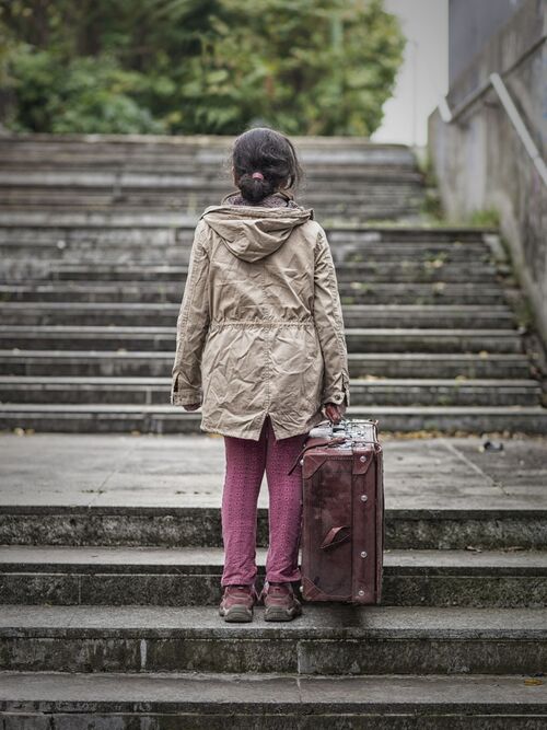 kleines Mädchen alleine auf einer Treppe mit einem Koffer