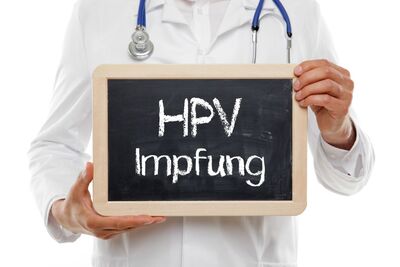 Mann im weißen Kittel mit Stethoskop hät ein Schild mit der Schrift HPV Impfung in der Hand