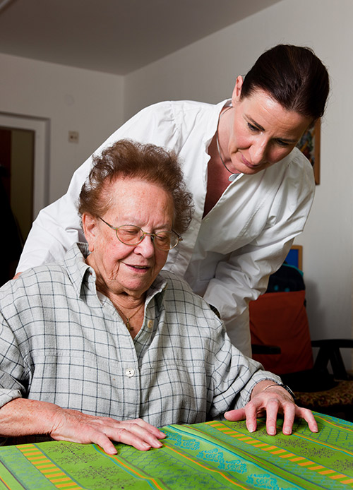Betreuerin hilft alter Frau beim Tisch