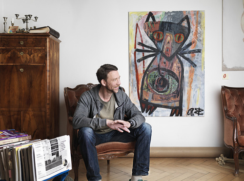 Mann sitzt auf einem Stuhl mit Kunstwerk im Hintergrund