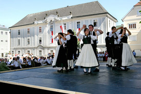 Tanzende Menschen in Tracht vorm Haus der Volkskultur