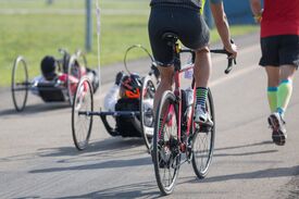 Zwei Sportler fahren auf einem Handbike neben einem Radfahrer und einem Läufer.