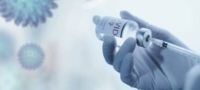 Eine Hand mit Schutzhandschuhen hält Impf-Serum-Fläschchen in der Hand