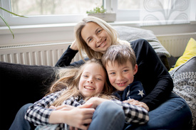 Mutter mit zwei Kindern sitzen auf der Couch und lachen in die Kamera