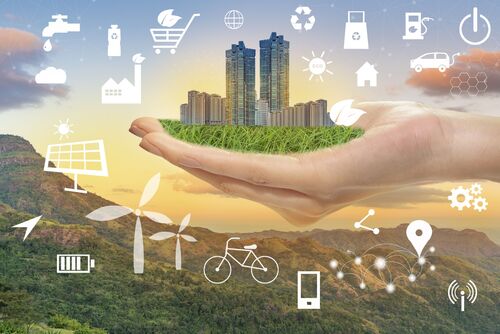 eine Hand hält auf einer Wiese Hochhäuser, umrandet von verschiedenen Grafikelementen zum Thema erneuerbare Energien (Windrad, Elektroauto, Fahrrad, Solarzelle usw.); im Hintergrund ist eine Berglandschaft zu sehen 