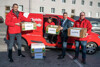 LR Wolfgang Hattmannsdorfer mit Jasmine Chansri und zwei Mitarbeiter der Volkshilfe stehen mit Pakete mit der Aufschrift „UKRAINE“ vor einem Volkshilfe-PKW auf einer Straße, dahinter ein langes Gebäude mit vielen Fenstern.