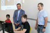 Landesrat Hattmannsdorfer und Szöky stehen hinter zwei Kindern, die auf einen Computer-Bildschirm schauen.