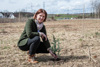 Landesrätin Michaela Langer-Weninger kniet bei einem frisch eingepflanzten Bäumchen auf einem Feld