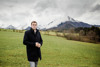 Landesrat Stefan Kaineder steht auf einer Wiese, im Hintergrund Wald und kaum schneebedeckte hohe Berge