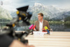 Landesrat Stefan Kaineder sitzt an einem Konferenztisch mit Mikrofonen, im Hintergrund ein Landschaftsbild mit See und Gebirge, im Vordergrund Kamera