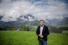 Landesrat Stefan Kaineder auf einer Wiese, im Hintergrund Berge