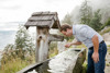 Landesrat Stefan Kaineder schöpft mit der Hand Wasser aus einem hölzernen Brunnentrog
