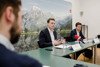 Landesrat Stefan Kaineder und Mag. Jürgen Frank sitzen nebeneinander an einem Konferenztisch, im Hintergrund an der Wand ein großes Foto von einer Berglandschaft mit See