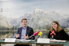 Landesrat Stefan Kaineder und Astrid Zeller sitzen nebeneinander an einem Konferenztisch, auf dem Unterlagen liegen und Mikrofone stehen, im Hintergrund eine Fotowand mit See und Berglandschaft