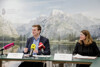 Landesrat Stefan Kaineder und Astrid Zeller sitzen nebeneinander an einem Konferenztisch, auf dem Unterlagen liegen und Mikrofone stehen, im Hintergrund eine Fotowand mit See und Berglandschaft