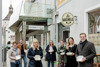 Elisabeth Kölbinger, Elias Gavino-Schlager, Eva De Michele, Bundesrätin Claudia Buschberger, Ulli Meinhart, Stadträtin Sonja Pickhardt-Kröpfel und Landesrat Stefan Kaineder auf dem Gehweg vor einem Restaurant, jeder hält eine Dose in Händen