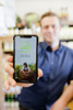 Landesrat Stefan Kaineder hält ein Smartphone in die Kamera, auf dem die App „Gutes Finden“ zu sehen ist, Beschriftung: Gutes Finden, Bild mit einem Mädchen, das auf einem Feld Gemüse erntet