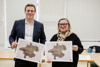 Landesrat Stefan Kaineder und Gudrun Achleitner-Kastner stehen nebeneinander in einem Konferenzraum, beide halten jeweils eine Karte in Händen