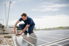 Landesrat Stefan Kaineder kniet auf einem Flachdach und schraubt an einem Solarpanel