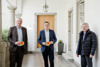 Geschäftsführender ÖVP-Klubobmann Dr. Christian Dörfel und Landesrat Stefan Kaineder mit dem oö. Anti-Atom-Beauftragten Dalibor Strasky in einem Arkadengang. Alle halten die Plakette „Atomstrom“ in den Händen.