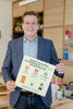 Landesrat Stefan Kaineder in einem Büroraum, er hält ein kleines Plakat in Händen mit der Beschriftung: Machen Sie aus Ihrer Veranstaltung einen Green-Event und gewinnen Sie