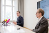 Landesrat Stefan Kaineder und Mag. Christoph Hofinger sitzen an einem Konferenztisch, Landesrat Stefan Kaineder spricht, vor ihm Mikrofone.