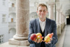 Landesrat Stefan Kaineder mit mehreren Äpfeln in Händen steht im Arkadengang des Linzer Landhauses  