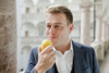 Landesrat Stefan Kaineder mit Apfel in der Hand steht im Arkadengang des Linzer Landhauses 