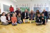 Bildungsreferentin LH-Stellvertreterin Christine Haberlander, Direktorin Lisa Slavulj, EducationGroup-GF Peter Eiselmair und Bürgermeister Markus Stadlbauer mit Schülerinnen und Schülern sowie Lehrinnern und Lehrern knien im Halbkreis in einem Klassenzimmer am Boden.