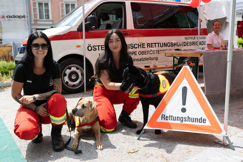Zwei Frauen mit zwei Rettungshunden bei einem Stand vor einem Einsatzwagen der Österreichischen Rettungshundebrigade. 