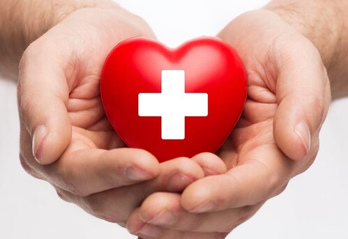 Symbol für Gesundheit und Hilfe: Hände halten ein Herz mit einem Kreuz