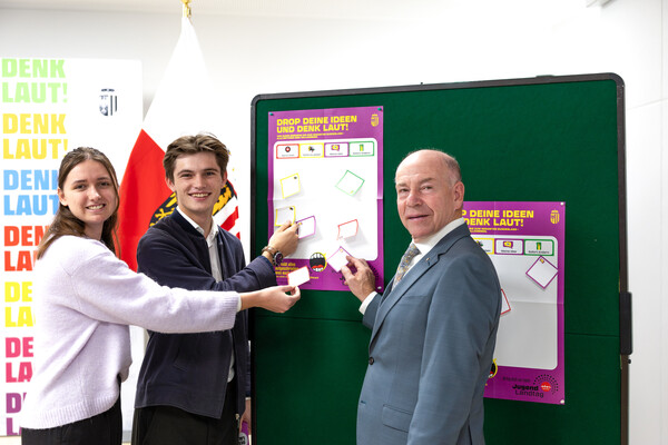 BMHS-Landesschulsprecherin Lorina Schneeberger, Jugendlandtagsteilnehmer 2025 Yannick Schmuch und Landtagspräsident Max Hiegelsberger stehen gemeinsam vor einer Pinwand und kleben vorerst noch leere Post-Its auf die Tafel. 