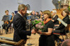 Landeshauptmann Mag. Thomas Stelzer überreicht Frau Prof.in Mag.a Mechthild Bartolomey einen Blumenstrauß, im Hintergrund ein klassisches Orchester