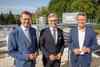 Landesrat Markus Achleitner, Finanzminister Magnus Brunner und Markus Mitteregger stehen nebeneinander, im Hintergrund eine Industrieanlage