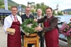 Landesrat Markus Achleitner mit Bieranstich-Hammer und Schürze, Hans Wieser, Wolfgang Eisl und Franz Eisl stehen nebeneinander um ein Bierfass, auf dem ein Kranz liegt, im Hintergrund See, Häuser, Kirche