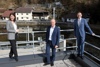 Dr.in Henrietta Egerth, Christoph Wagner und Landesrat Markus Achleitner auf einer Terrasse über einem Staubereich, am Ufer Häuser