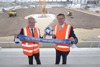 v.l.: Wirtschafts- und Sport-Landesrat Markus Achleitner und Bürgermeister Klaus Luger stehen miteinander auf der Baustelle des Stadions von Blau-Weiß Linz, im Hintergrund Baufahrzeuge in der künftigen Arena, die beiden halten einen Fan-Schal und einen Fußball in den Vereinsfarben von Blau Weiß Linz in den Händen.
