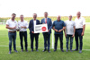 Christian Sturmair, Franz Schiefermair, Christian Schöffmann, Landesrat Markus Achleitner, Gerhard Walter, Helmut Oberndorfer und Josef Sturmair stehen nebeneinander auf einem Fußballfeld, Landesrat Achleitner hält ein Schild mit Beschriftung Infrastrukturoffensive Sport Oberösterreich